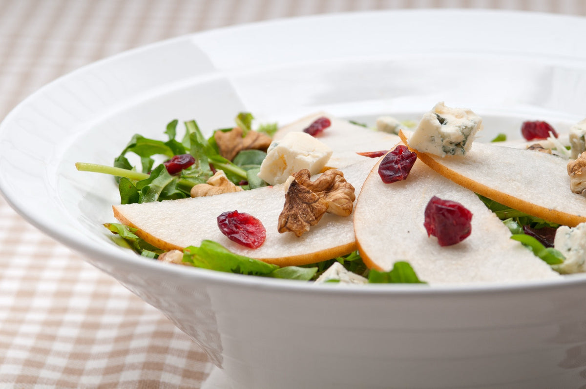 Pear and arugula salad with Gorgonzola, walnuts and dried cranberries in a white bowl