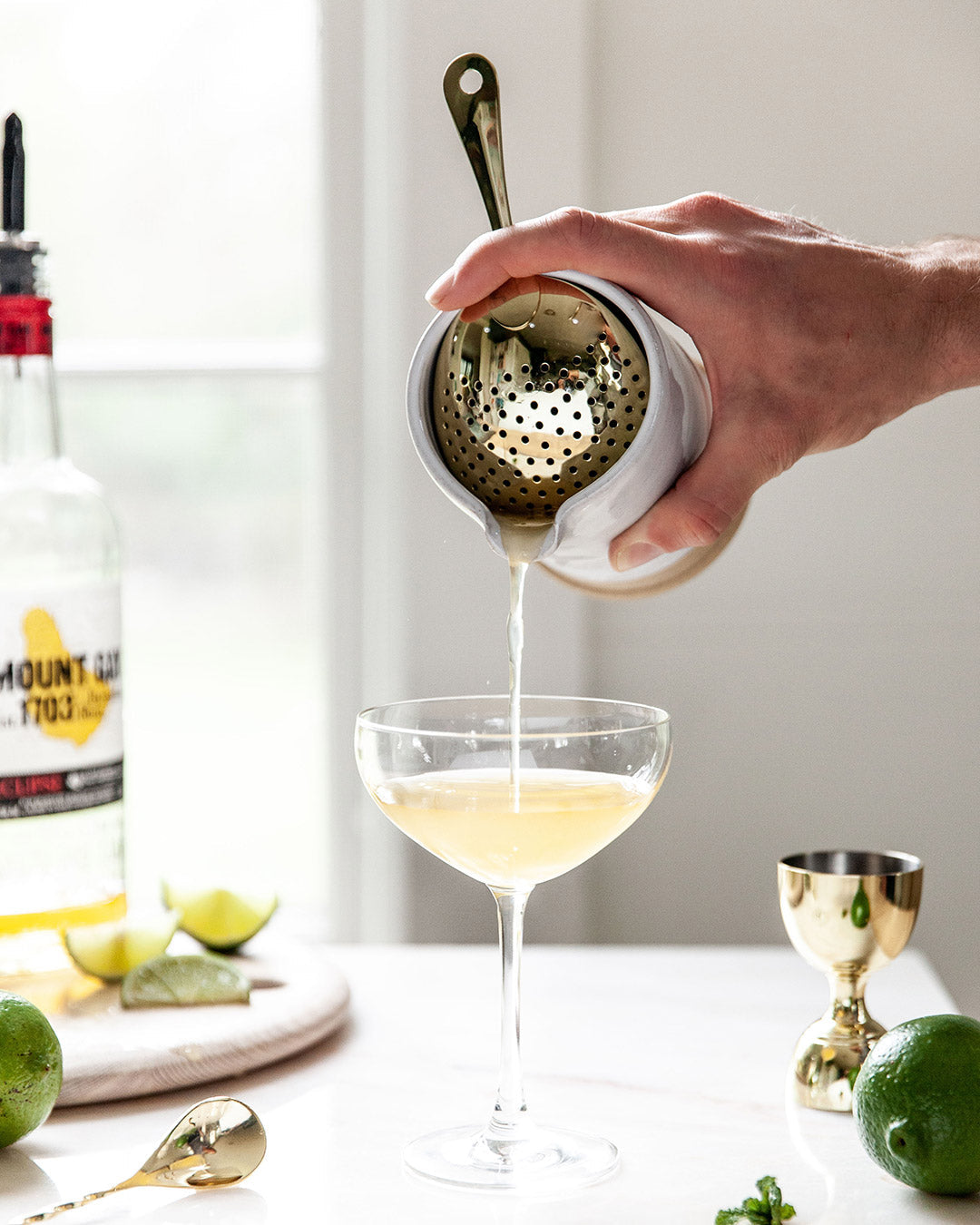 A cocktail being poured from the Countryman Cocktail Beaker through a strainer into a coupe glass