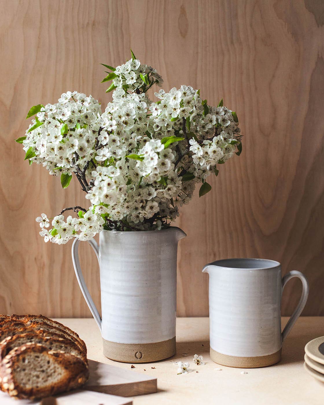 Farmhouse Pottery Silo Pitchers styled with white flowering branches and rustic bread; pitchers are sold individually and flowers and accessories are not included.