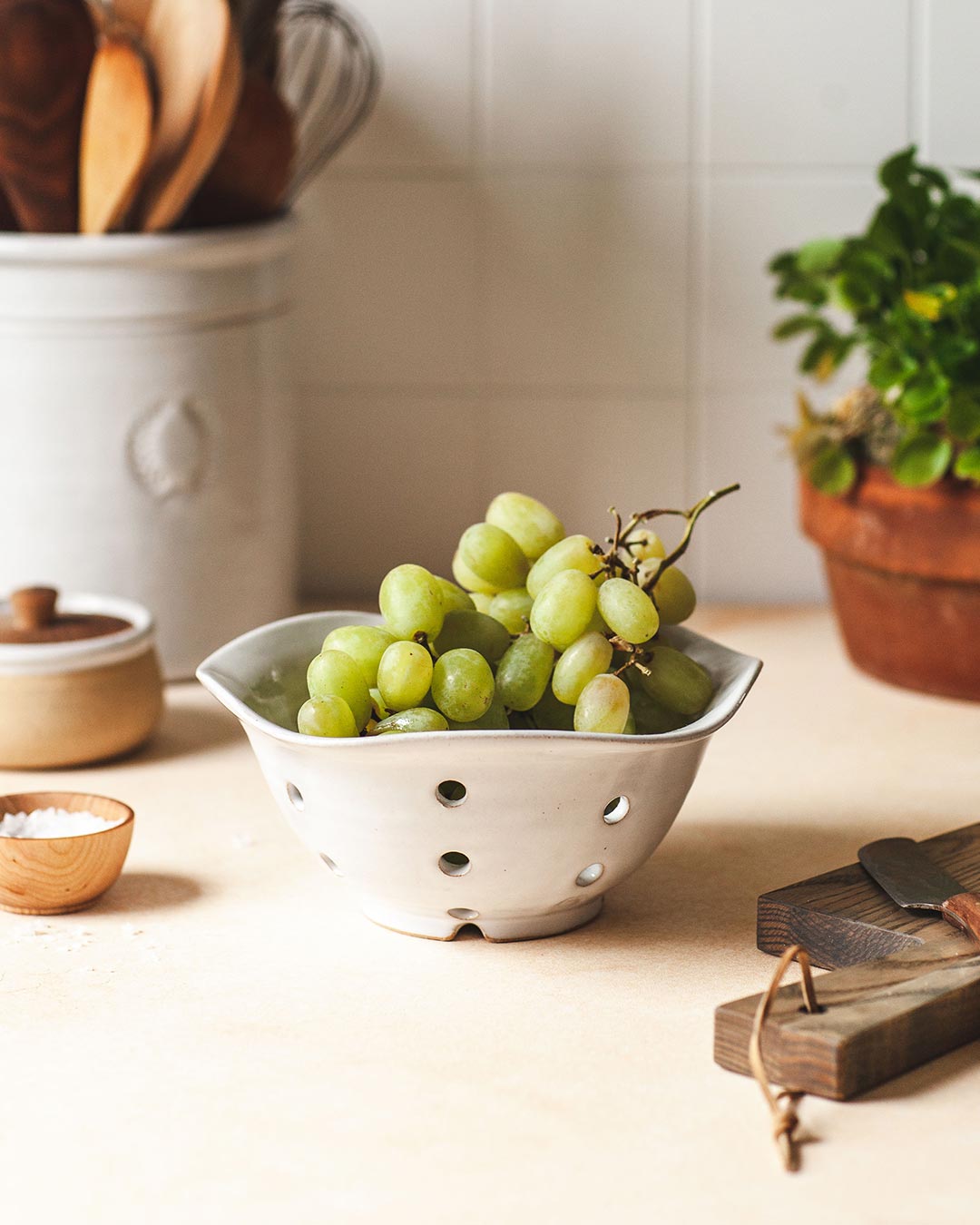 Farmhouse Pottery Windrow Berry Bowl holding green grapes on a kitchen counter; fruit and styling accessories not included.