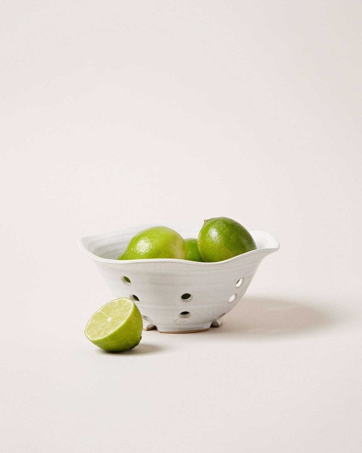 Farmhouse Pottery Windrow Berry Bowl styled with fresh green limes, showing the white glaze and drainage holes; limes not included.