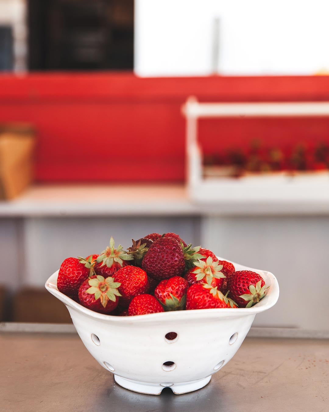 White Farmhouse Pottery Windrow Berry Bowl displaying strawberries on a counter, showing its perforated sides and footed base; fruit not included.